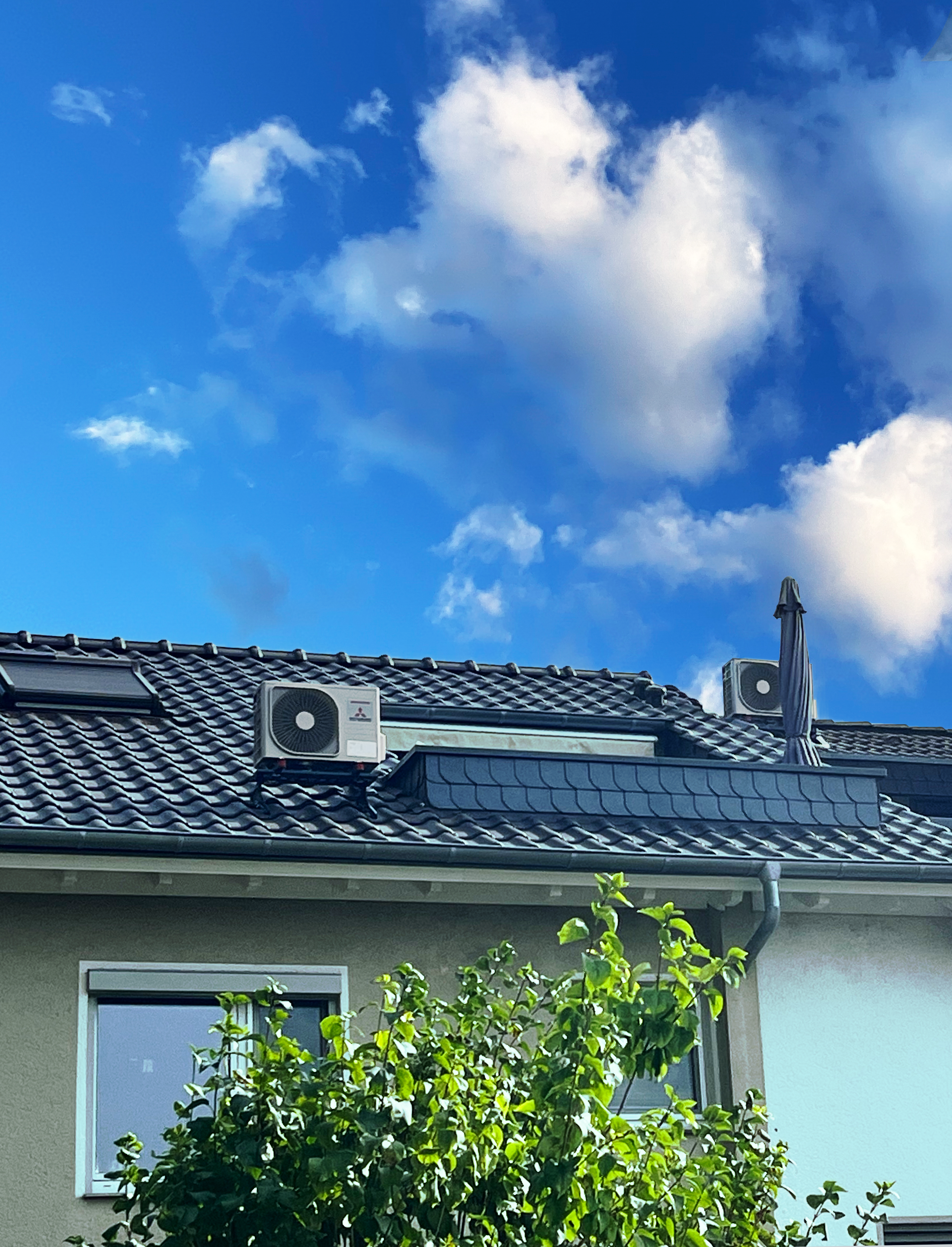 Ein Haus, auf dessen Dach zwei Außengeräte der Mitsubishi-Klimaanlagen stehen. Es ist ein sonniger Tag, man sieht Grün im Vordergrund.